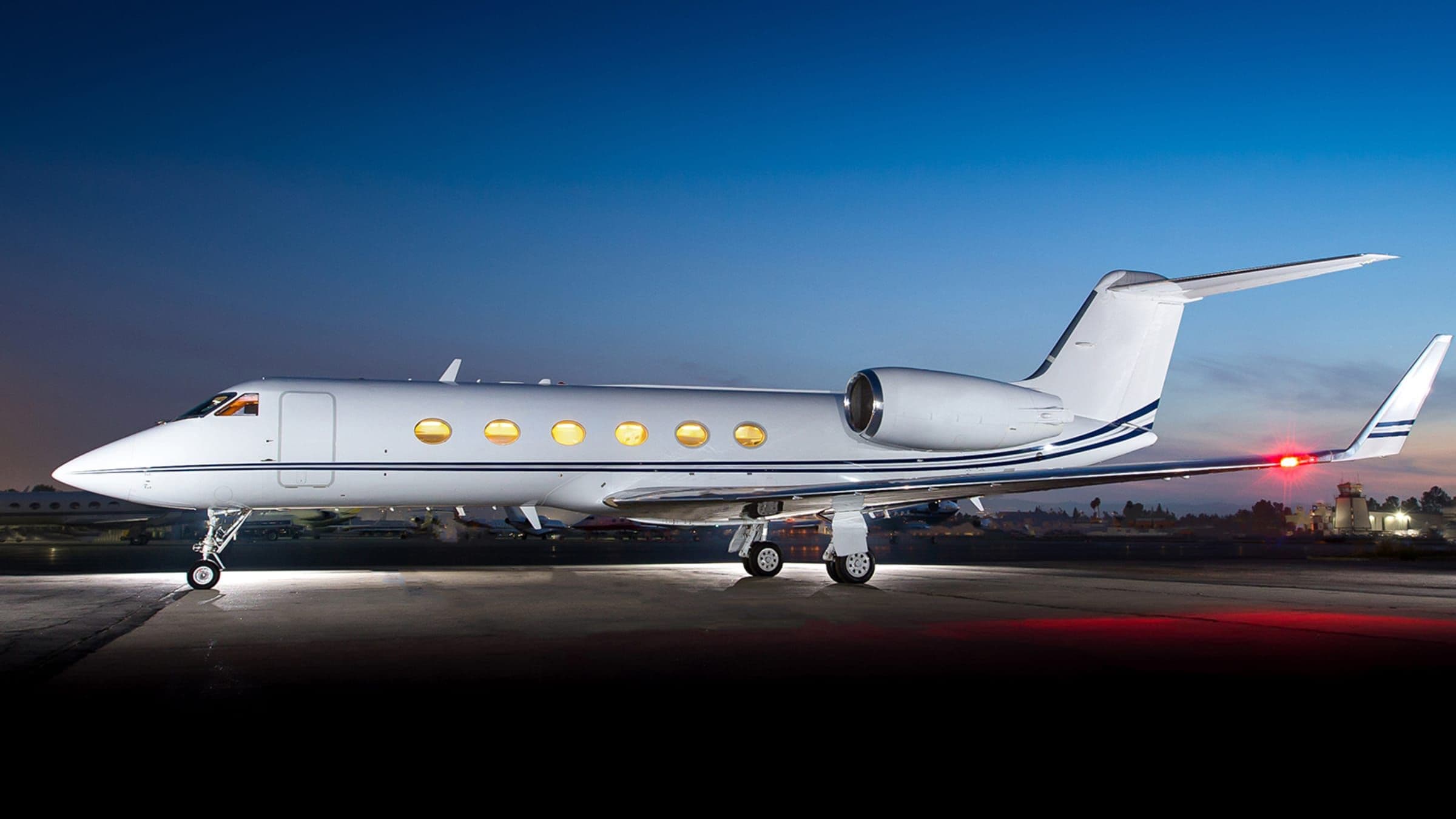 Gulfstream GIV on a floodlit ramp at dusk, cabin windows lit